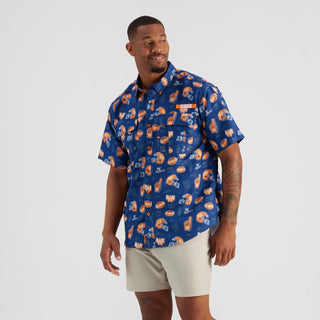 Man wearing a blue patterned shirt and beige shorts on a white background