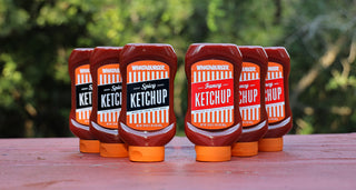 View fancy and spicy ketchup three packs on a red bench with trees behind them.