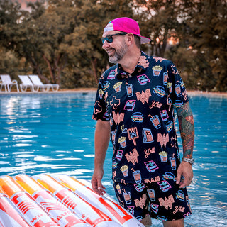 view model wearing whataburger chubbies polo and swim trunks in a pool with wooded area in the background.