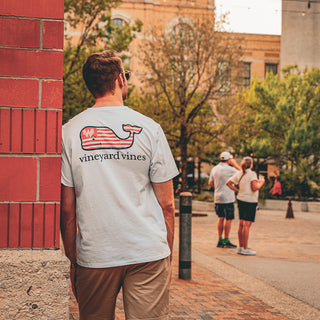 man wearing vineyard vines leaning against a brick wall in a crowded farmers market.