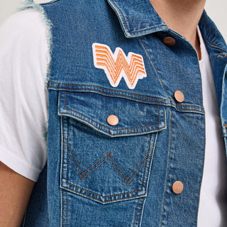 Front detail of the Wrangler® x Whataburger® Men's Cut-Off Vest – A male model wears the Wrangler® x Whataburger® Men's Cut-Off Vest, featuring a classic blue denim design with frayed armholes, copper buttons, and contrast stitching. The vest has an embroidered Flying W patch on the chest and a rodeo-style embroidered patch below it.