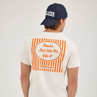 The model shows the back of the Wrangler® x Whataburger® Just Like You Like It T-Shirt, featuring an orange and white striped design with the phrase "Denim. Just Like You Like It." centered inside an oval. He pairs it with Wrangler jeans and a navy blue cap with "Long Live Burgers."