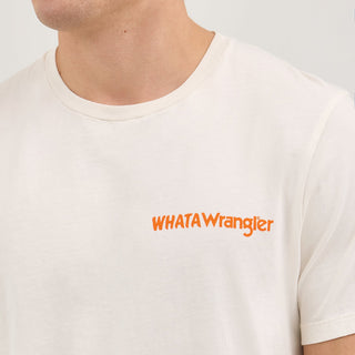 A male model wears the Wrangler® x Whataburger® Just Like You Like It T-Shirt in off-white. The t-shirt features a small "WHATAWrangler" logo in orange on the left chest. He pairs it with blue denim jeans and classic sneakers, standing in a relaxed pose.