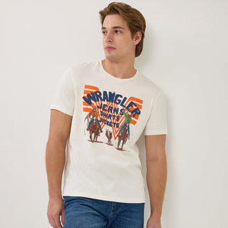 Front View: A male model leans casually against a white wall wearing the Wrangler® x Whataburger® White Graphic T-Shirt. The shirt features a vintage-style rodeo graphic with two cowboys on horseback and a cow, set against an orange and blue Flying W design. He pairs the shirt with classic blue jeans and cowboy boots.