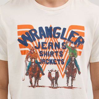 Close-up Front Design: A detailed shot of the Wrangler® x Whataburger® White Graphic T-Shirt's design. The print features two cowboys on horseback, one in a yellow and orange outfit, the other in green, with a cow running between them. The graphic is framed by a bold orange Flying W with the text "Wrangler Jeans Shirts Jackets" in blue.