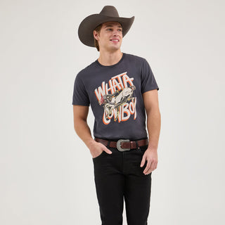 A male model wearing the Wrangler® x Whataburger® Cowboy Graphic Black T-Shirt, styled with black jeans, a brown belt, and cowboy boots. The front design features a distressed illustration of a cowboy riding a bucking horse, with the bold text "WHATA COWBOY" in orange and white.