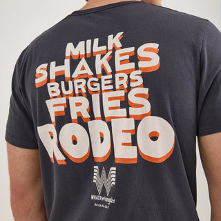 A close-up of the back of the Wrangler® x Whataburger® Cowboy Graphic Black T-Shirt. The back design includes large, stacked text reading "MILK SHAKES BURGERS FRIES RODEO" in a bold Western-style font with an orange and white outline. Below, the Whataburger Flying W logo appears with the tagline "Just Like You Like It."