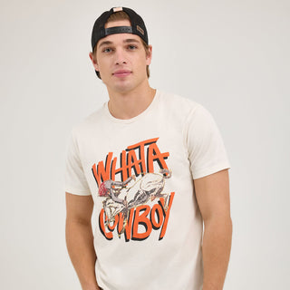 A male model wears the Wrangler® x Whataburger® Cowboy Graphic White T-Shirt with a "WHATA COWBOY" bronc-riding graphic on the front. He pairs it with blue jeans and a black mesh-back cap, standing in a relaxed pose.