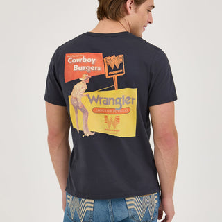 A model facing away from the camera, highlighting the detailed graphic on the back of the Wrangler® x Whataburger® Cowboy Burgers Black T-Shirt. The design includes nostalgic Western elements and bold typography in Whataburger's signature orange.