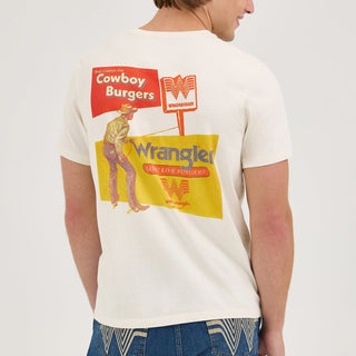 A male model showcasing the back design of the Wrangler® x Whataburger® Cowboy Burgers White T-Shirt. The vintage-style graphic features a cowboy lassoing with a Whataburger® sign, and retro-inspired typography reading "Real Cowboys Eat Cowboy Burgers."