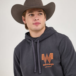 A male model wearing the Wrangler® x Whataburger® Faded Black Hoodie and a cowboy hat, looking off to the side. The hoodie features the Flying W logo and "WHATAWrangler" text in orange on the chest.