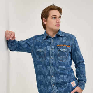 Front view of the Wrangler® x Whataburger® Men's Western Print Shirt – A male model wears the Wrangler® x Whataburger® Men's Western Print Shirt, featuring an all-over Flying W pattern on blue denim, pearl snap buttons, and chest pockets with contrast stitching. The "WHATAWrangler" embroidery is displayed above the left pocket.