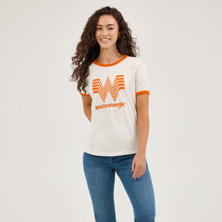 The model stands tall, displaying the Wrangler® x Whataburger® Women's Ringer Tee paired with high-waisted blue jeans and brown cowboy boots. The outfit reflects a casual yet Western-inspired aesthetic.