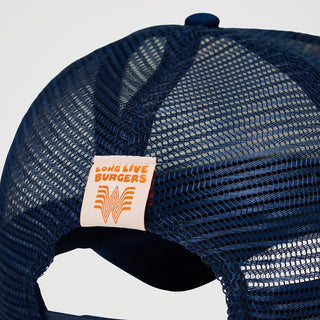 A close-up of the back of the Wrangler® x Whataburger® Foam Navy Trucker Hat, featuring a navy mesh design with an adjustable snapback closure. A small beige tag with orange "LONG LIVE BURGERS" text and the Whataburger "W" logo is stitched onto the back.