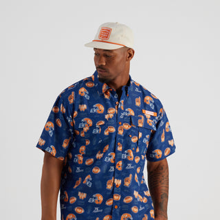 Man wearing a blue patterned shirt and white cap on a gray background