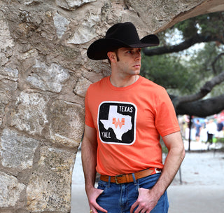 View man wearing Whataburger Orange Texas Road Sign Tee leaning on an archway. Reads Apparel.