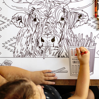 Child coloring a black and white cow illustration with markers