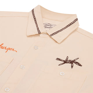 Beige shirt with brown embroidery and text on a white background
