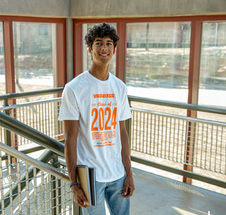 view student wearing the class of '24 tee while standing in a stairwell holding books.