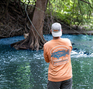 view man fishing in a river wearing the peach whataburger fishing club uv long sleeve tee and whatadad hat.