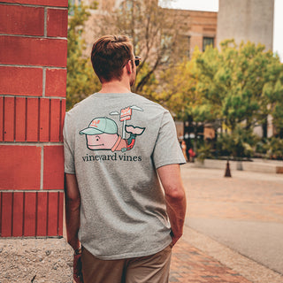 man wearing vineyard vines leaning against a brick wall in a crowded farmers market.