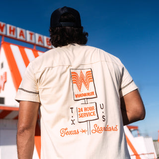 Person wearing a white shirt with a Whataburger logo, standing in front of a Whataburger restaurant.