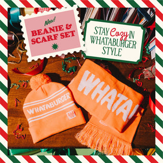 Orange beanie and scarf set with 'WHATA!' branding on a wooden surface, surrounded by festive decorations.