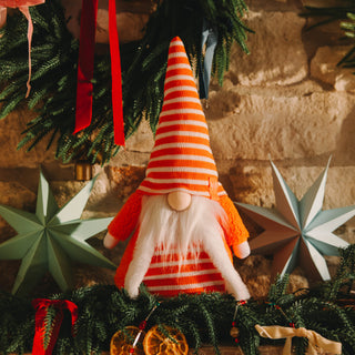 Decorative gnome with striped hat among Christmas decorations on a stone wall background
