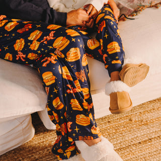 Person wearing navy pajama pants with Whataburger breakfast pattern sitting on a white couch.