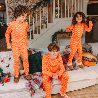 Three children in matching orange Whataburger pajamas sitting on a couch in a cozy living room.