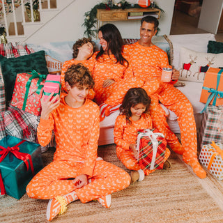 Family in matching orange Whataburger pajamas sitting on a couch surrounded by Christmas presents.