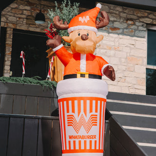 Inflatable reindeer decoration with Whataburger logo in front of a stone building.