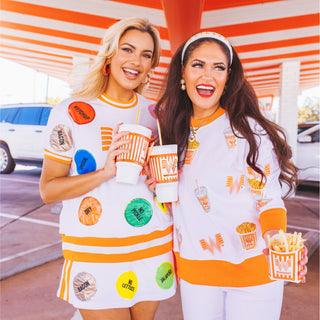 Two women in Brianna Cannon x Whataburger outfits standing in front of a striped building.
