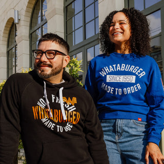 A man and woman wearing Whatburger-branded outerwear standing against a building facade