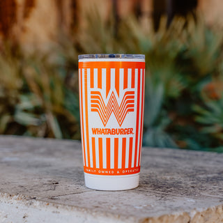 An orange and white striped 20oz Whataburger Yeti Rambler® tumbler with a stainless steel base, featuring the iconic Whataburger 'W' logo and text engraved on the surface, placed on a stone surface with a blurred natural background.