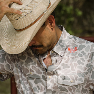 A man wearing a light beige straw cowboy hat and a Classic Deer Camo pattern button down shirt and an orange Whataburger logo embroidered logo on the chest pocket.
