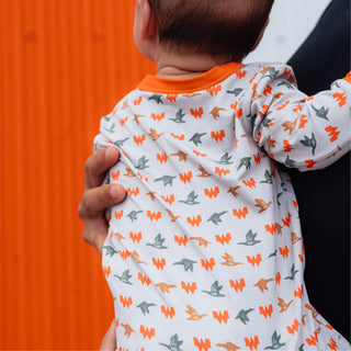 Baby held up in front of orange and white striped building wearing WHATA Mallard Baby Zip Up.