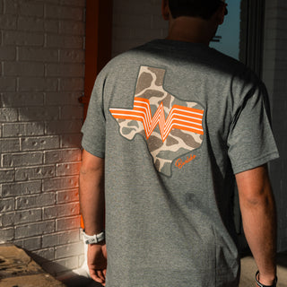 A man viewed from behind wearing a heather gray t-shirt with a large graphic on the back. The graphic features the state outline of Texas filled with a Classic Deer Camo pattern, overlaid with orange and white Whataburger logo, and a small orange script Burlebo logo near the bottom right.