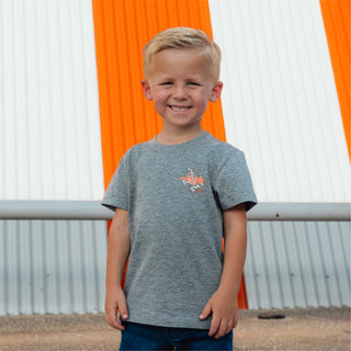 Smiling child wearing Youth WHATA Texas Tee in front of orange and white striped Whataburger A-Frame building.