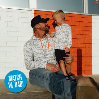 Father sitting in front of orange and white striped brick wall with son wearing matching Youth White Camo Performance Hoodies and circular callout reading 'Match with Dad!'