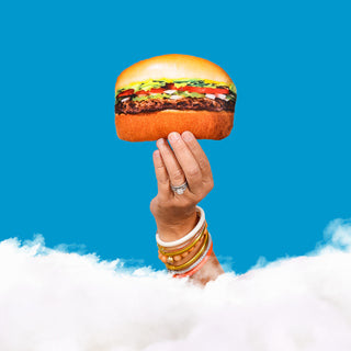 Hand holding a Mini #1 Burger Pillow above clouds with a blue sky background