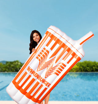 Person holding a large inflatable Whataburger cup by a pool
