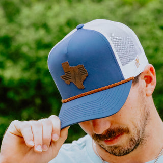 Man wearing a blue and white cap with a Texas-shaped logo, outdoors.