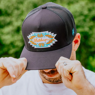 Person holding a black cap with a colorful logo against a blurred green background