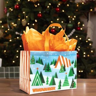 Whataburger holiday gift bag featuring snowy Christmas trees, an A-frame restaurant and orange tissue paper.