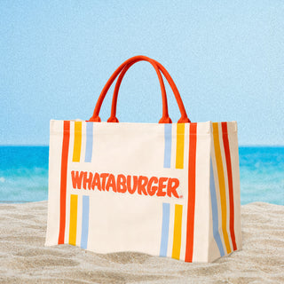 Striped canvas bag with 'Whataburger' logo sitting on a sandy beach with ocean view