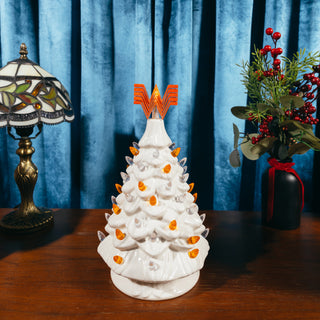 View Whataburger White Ceramic Tree alongside holiday lamp and floral decoration. Sitting on wooden surface in front of blue curtain. 