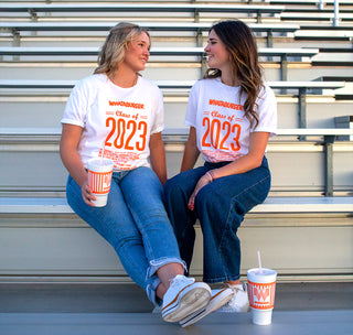View two students sitting on bleachers wearing the class of 23 tee.