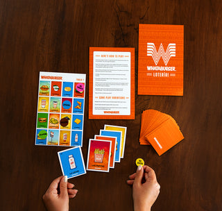 View hands over a wooden table setting up a whataburger loteria game.