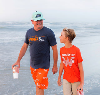 View father and son walking down beach wearing whataburger clothing.